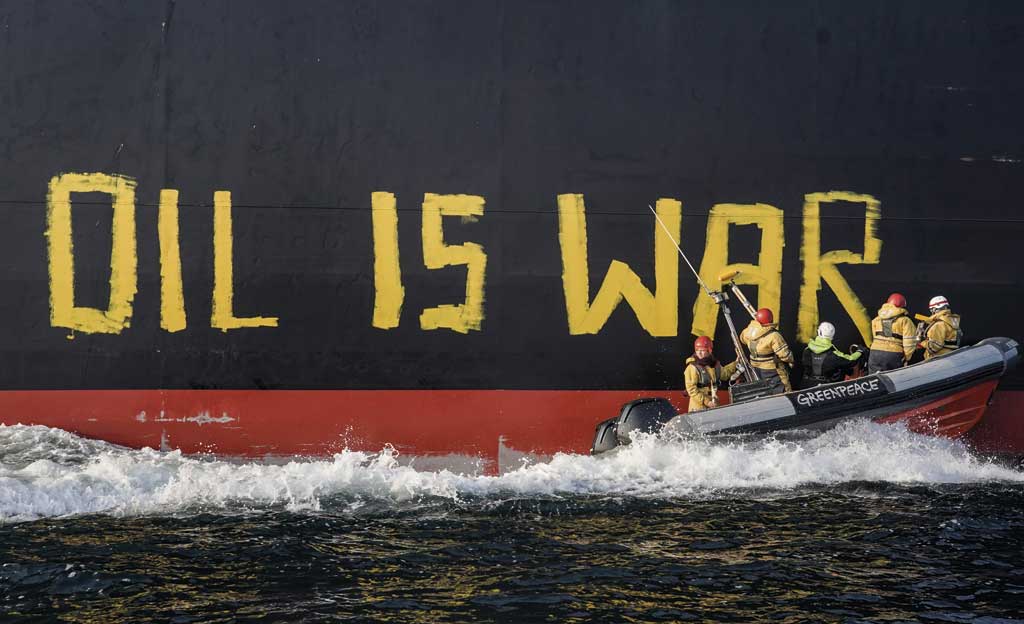 Activistas en una embarcación pintan sobre el casco de un petrolero la frase: OIL IS WAR