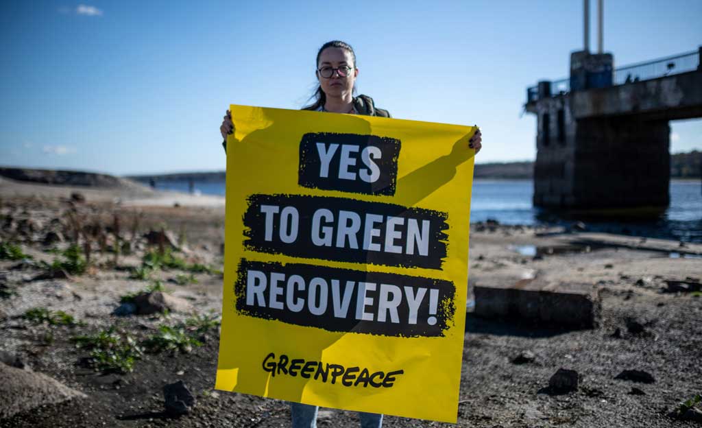 Activista de Greenpeace en una playa sostiene un cartel con la frase: YES TO GREEN RECOVERY