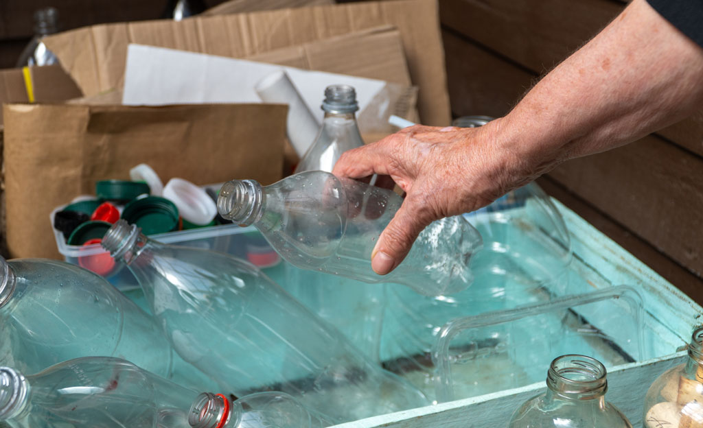 La mano de una persona mayor recicla botellas de plástico