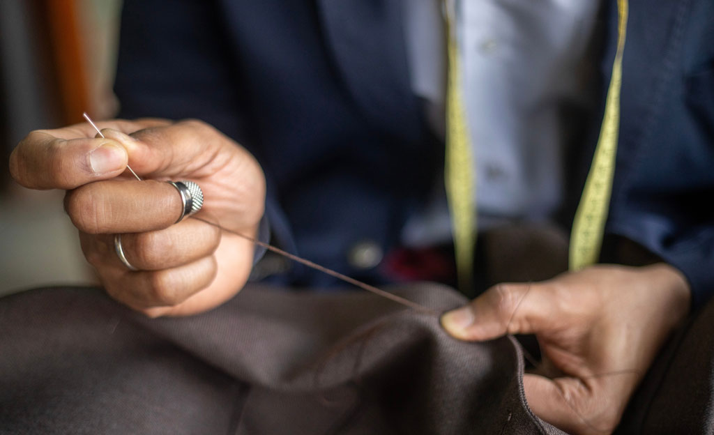 Las manos de un hombre mayor con un dedal cosiendo un traje.