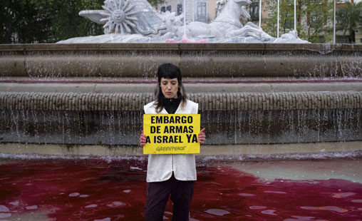 Activista de Greenpeace en la fuenta de Neptuno donde han teñido el agua de color rojo mientras sostiene una pancarta que dice EMBARGO DE ARMAS A ISRAEL YA