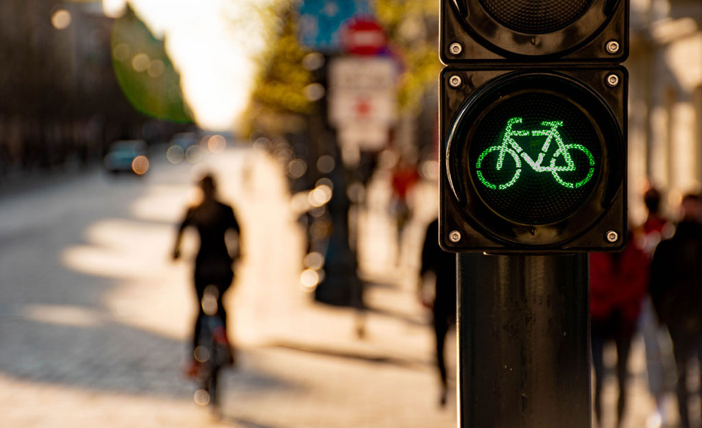 Semáforo para bicicletas en verde. Al fondo puede verse a una ciclista en un carril bici.